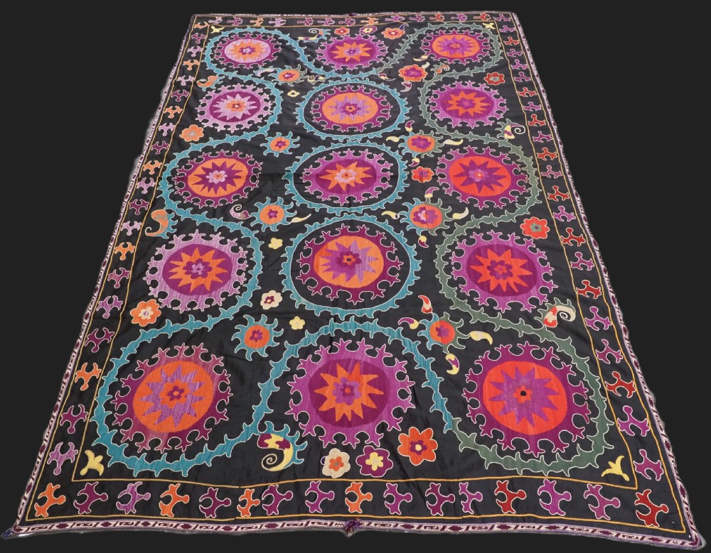 An antique Uzbek suzani textile featuring vibrant purple, orange, and teal silk embroidery in medallion patterns across a black cotton ground.