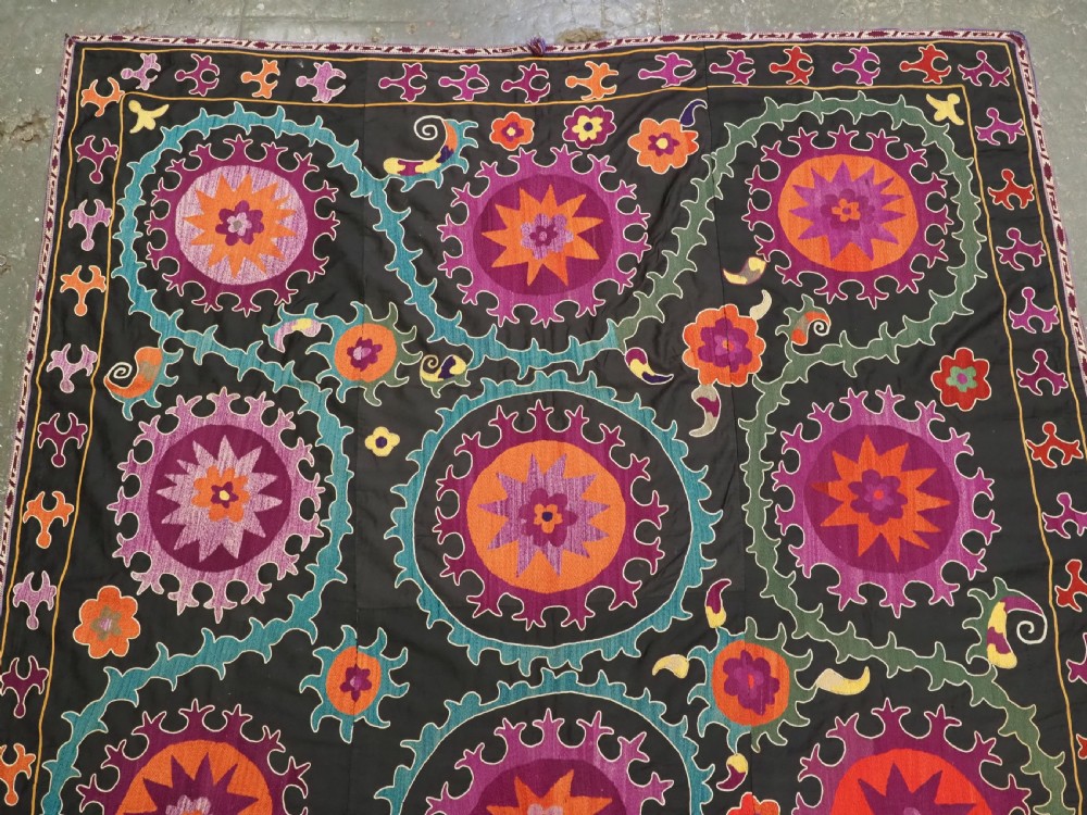 An antique Uzbek suzani textile featuring vibrant purple, orange, and teal silk embroidery in medallion patterns across a black cotton ground. View II