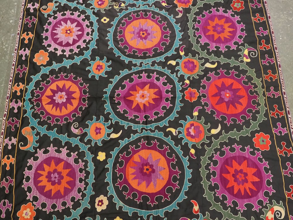 An antique Uzbek suzani textile featuring vibrant purple, orange, and teal silk embroidery in medallion patterns across a black cotton ground. View III