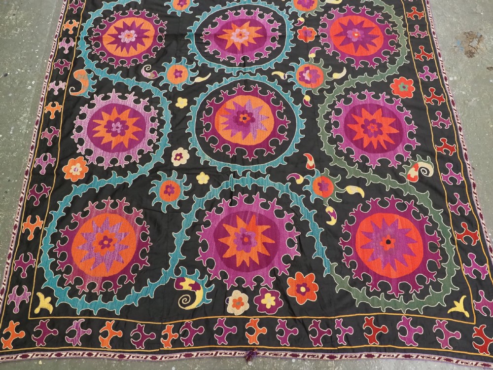 An antique Uzbek suzani textile featuring vibrant purple, orange, and teal silk embroidery in medallion patterns across a black cotton ground. View IV