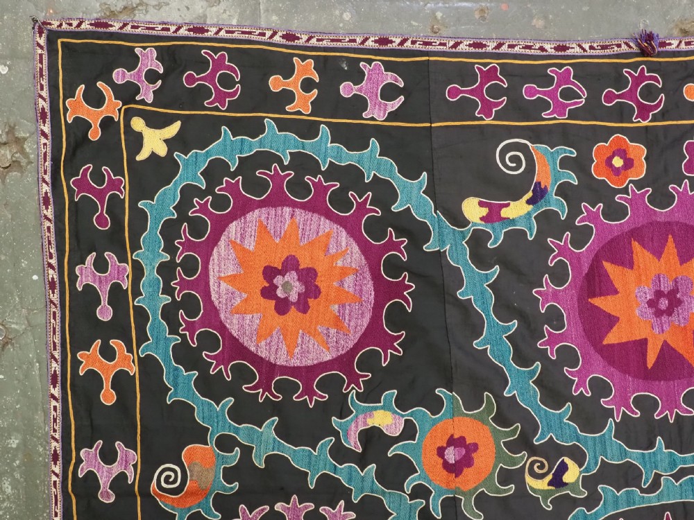 An antique Uzbek suzani textile featuring vibrant purple, orange, and teal silk embroidery in medallion patterns across a black cotton ground. View V