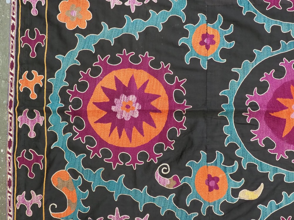 An antique Uzbek suzani textile featuring vibrant purple, orange, and teal silk embroidery in medallion patterns across a black cotton ground. View VI