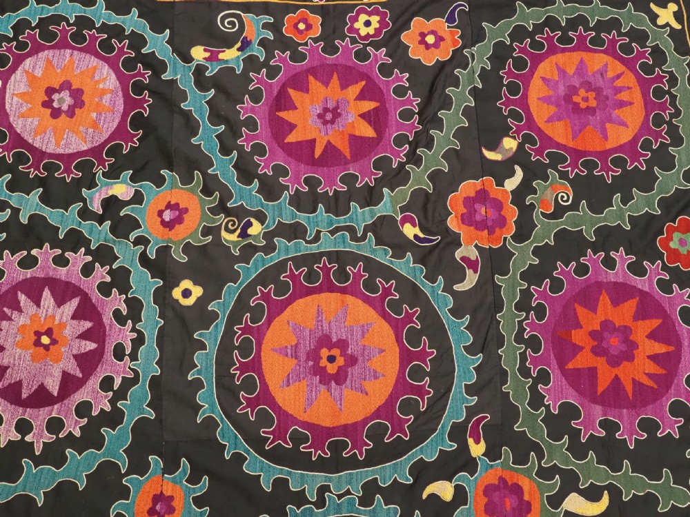 An antique Uzbek suzani textile featuring vibrant purple, orange, and teal silk embroidery in medallion patterns across a black cotton ground. View VII