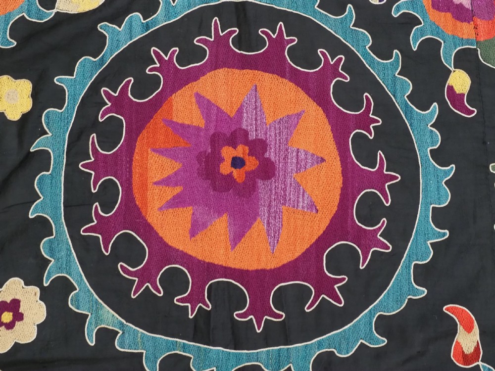 An antique Uzbek suzani textile featuring vibrant purple, orange, and teal silk embroidery in medallion patterns across a black cotton ground. View IX