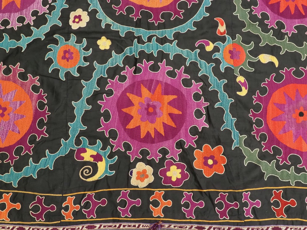 An antique Uzbek suzani textile featuring vibrant purple, orange, and teal silk embroidery in medallion patterns across a black cotton ground. View X
