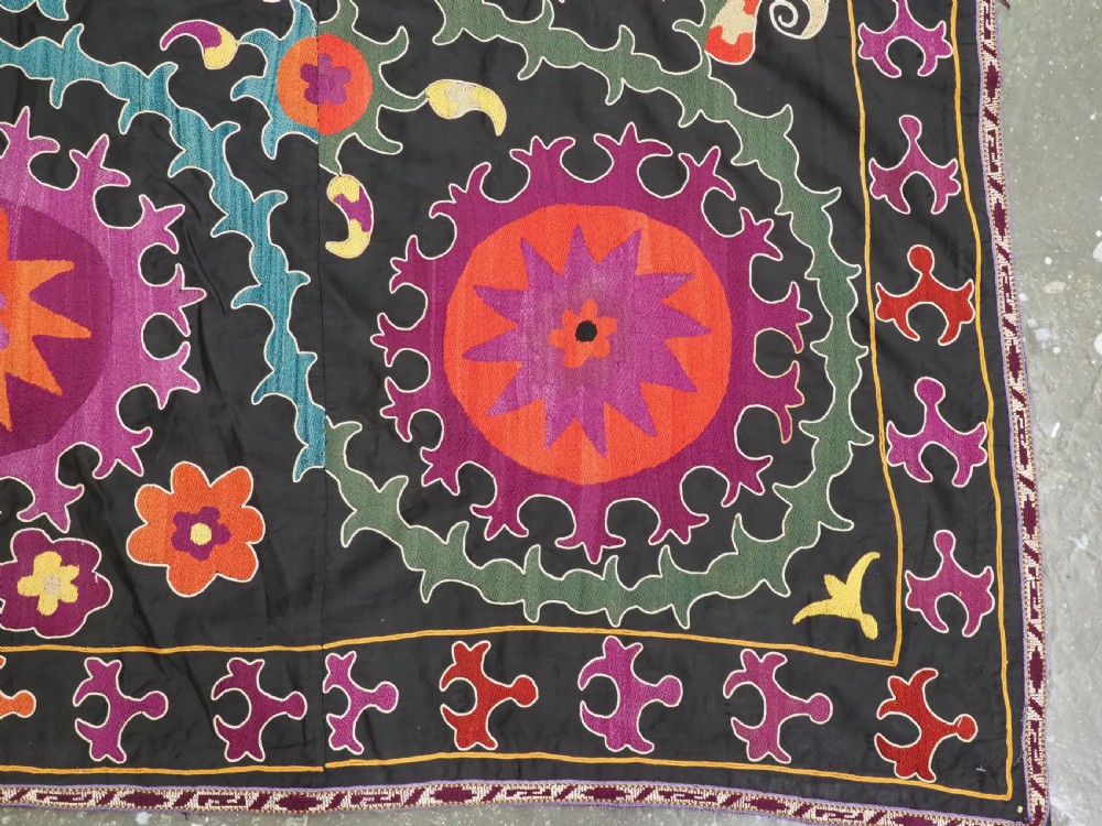 An antique Uzbek suzani textile featuring vibrant purple, orange, and teal silk embroidery in medallion patterns across a black cotton ground. View XI