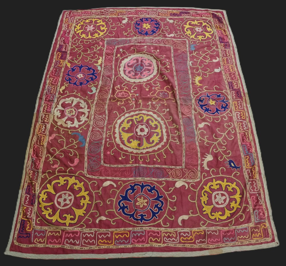 A rectangular magenta pink cotton textile embroidered with circular floral medallions in yellow, blue, and white silk threads.