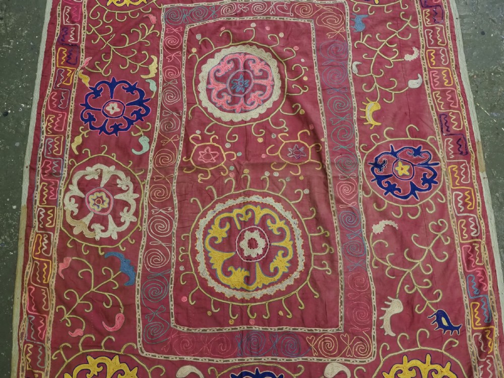 A rectangular magenta pink cotton textile embroidered with circular floral medallions in yellow, blue, and white silk threads. View III