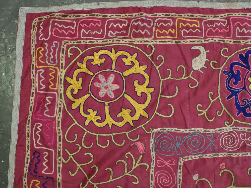 A rectangular magenta pink cotton textile embroidered with circular floral medallions in yellow, blue, and white silk threads. View V