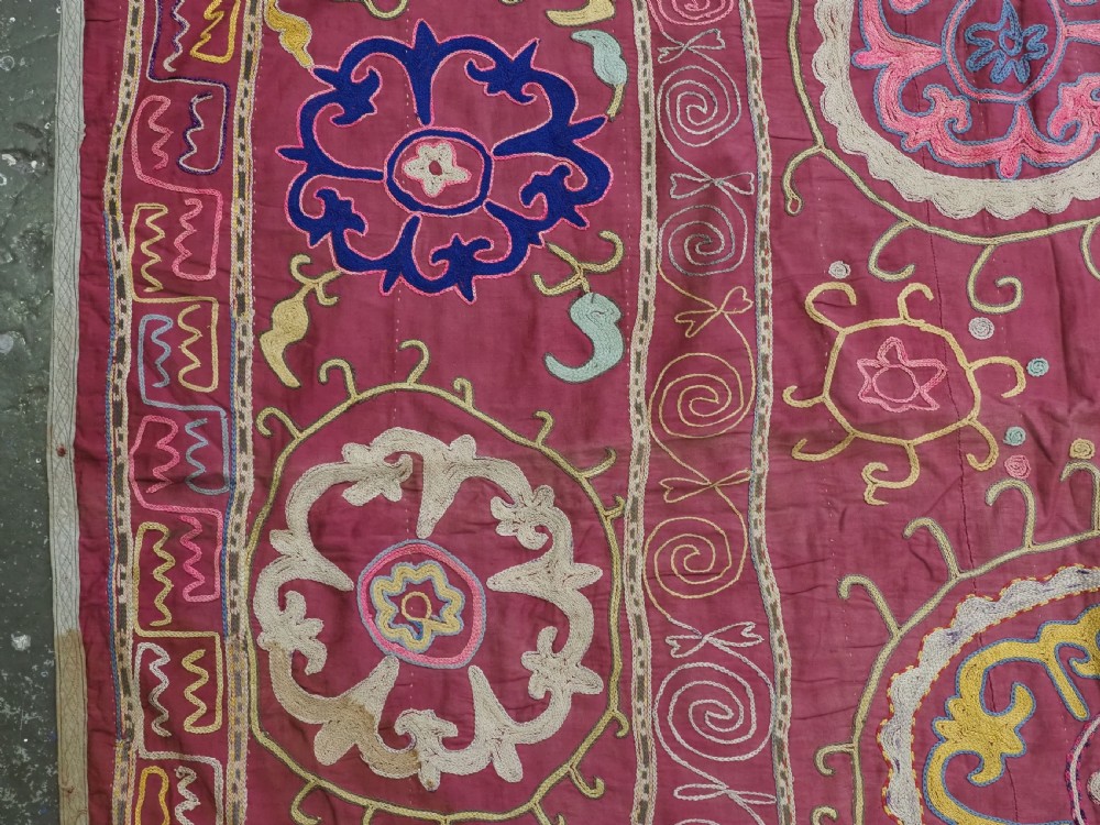 A rectangular magenta pink cotton textile embroidered with circular floral medallions in yellow, blue, and white silk threads. View VI