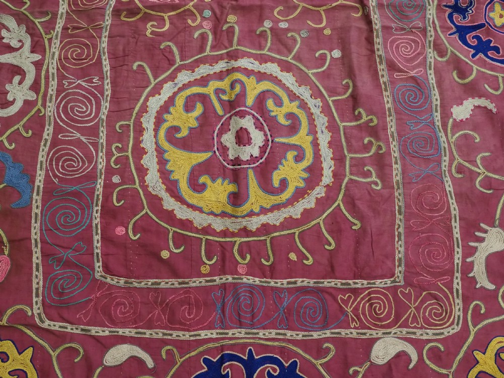 A rectangular magenta pink cotton textile embroidered with circular floral medallions in yellow, blue, and white silk threads. View IX