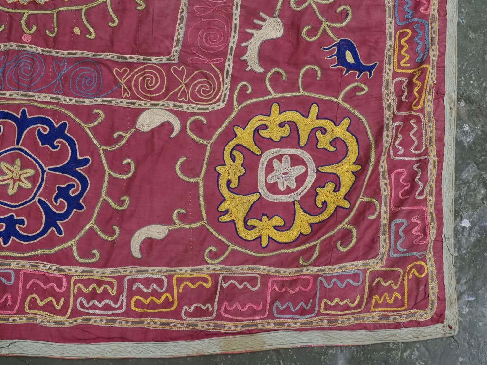 A rectangular magenta pink cotton textile embroidered with circular floral medallions in yellow, blue, and white silk threads. View X