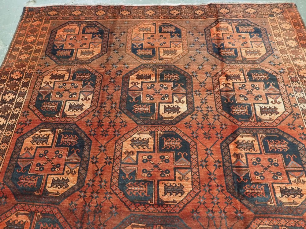 An antique northern Afghan Ersari Turkmen wool carpet featuring repeating octagonal gul motifs in dark blue, beige, and brown set against a deep terracotta red field. View III