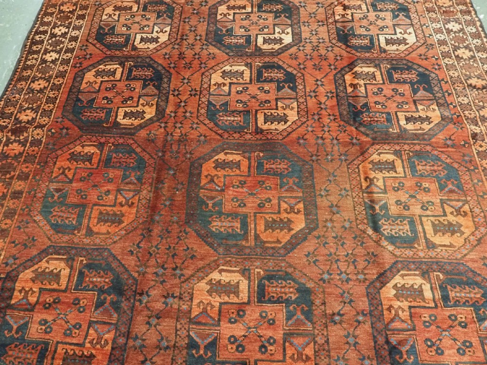 An antique northern Afghan Ersari Turkmen wool carpet featuring repeating octagonal gul motifs in dark blue, beige, and brown set against a deep terracotta red field. View IV