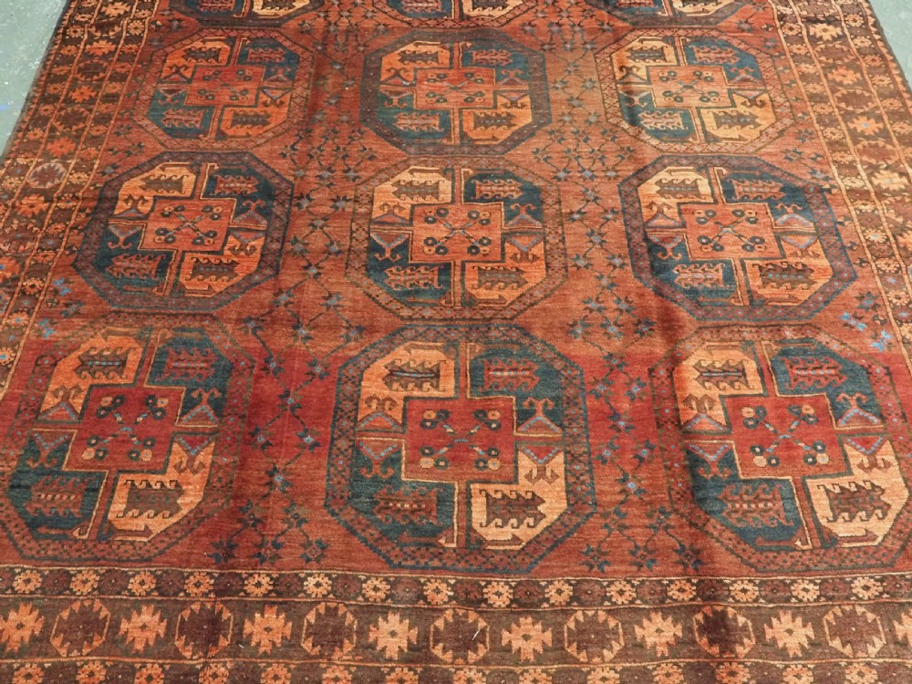 An antique northern Afghan Ersari Turkmen wool carpet featuring repeating octagonal gul motifs in dark blue, beige, and brown set against a deep terracotta red field. View V