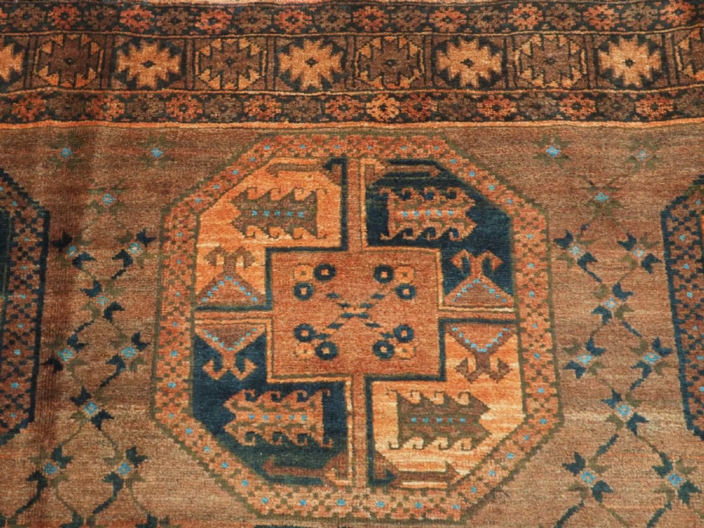 An antique northern Afghan Ersari Turkmen wool carpet featuring repeating octagonal gul motifs in dark blue, beige, and brown set against a deep terracotta red field. View VIII