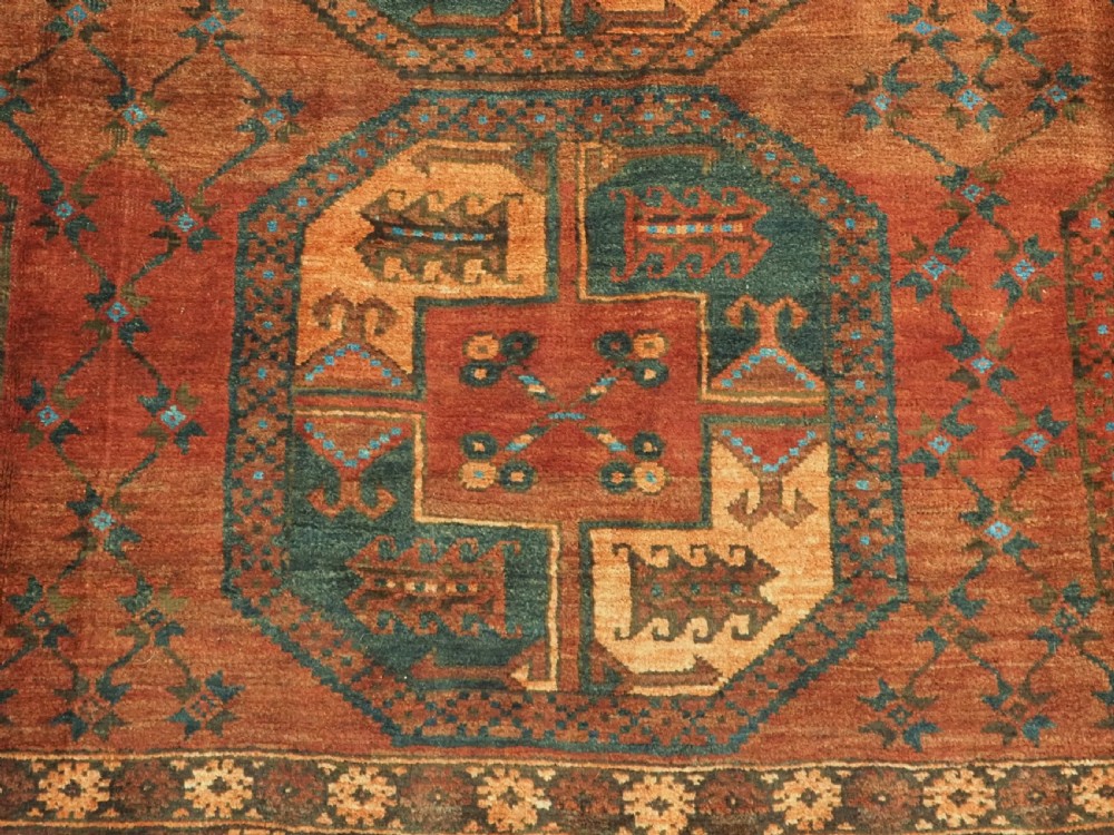 An antique northern Afghan Ersari Turkmen wool carpet featuring repeating octagonal gul motifs in dark blue, beige, and brown set against a deep terracotta red field. View X