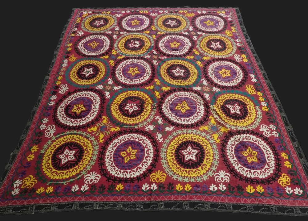 A rectangular hand-embroidered Uzbek suzani textile featuring circular solar medallions with central stars in shades of yellow, purple, white, and red.