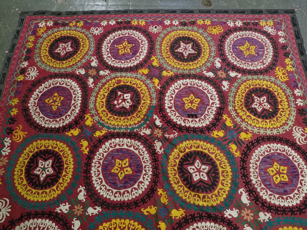 A rectangular hand-embroidered Uzbek suzani textile featuring circular solar medallions with central stars in shades of yellow, purple, white, and red. View II