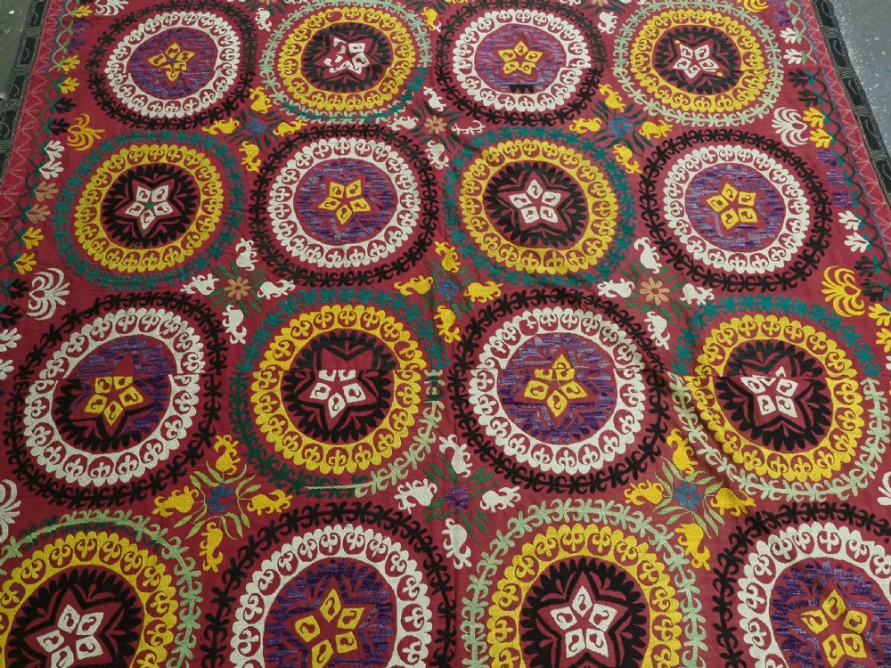 A rectangular hand-embroidered Uzbek suzani textile featuring circular solar medallions with central stars in shades of yellow, purple, white, and red. View III