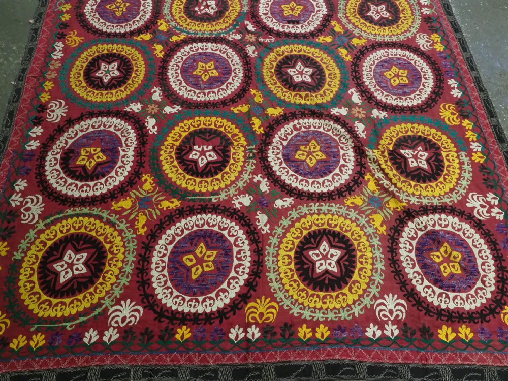 A rectangular hand-embroidered Uzbek suzani textile featuring circular solar medallions with central stars in shades of yellow, purple, white, and red. View IV