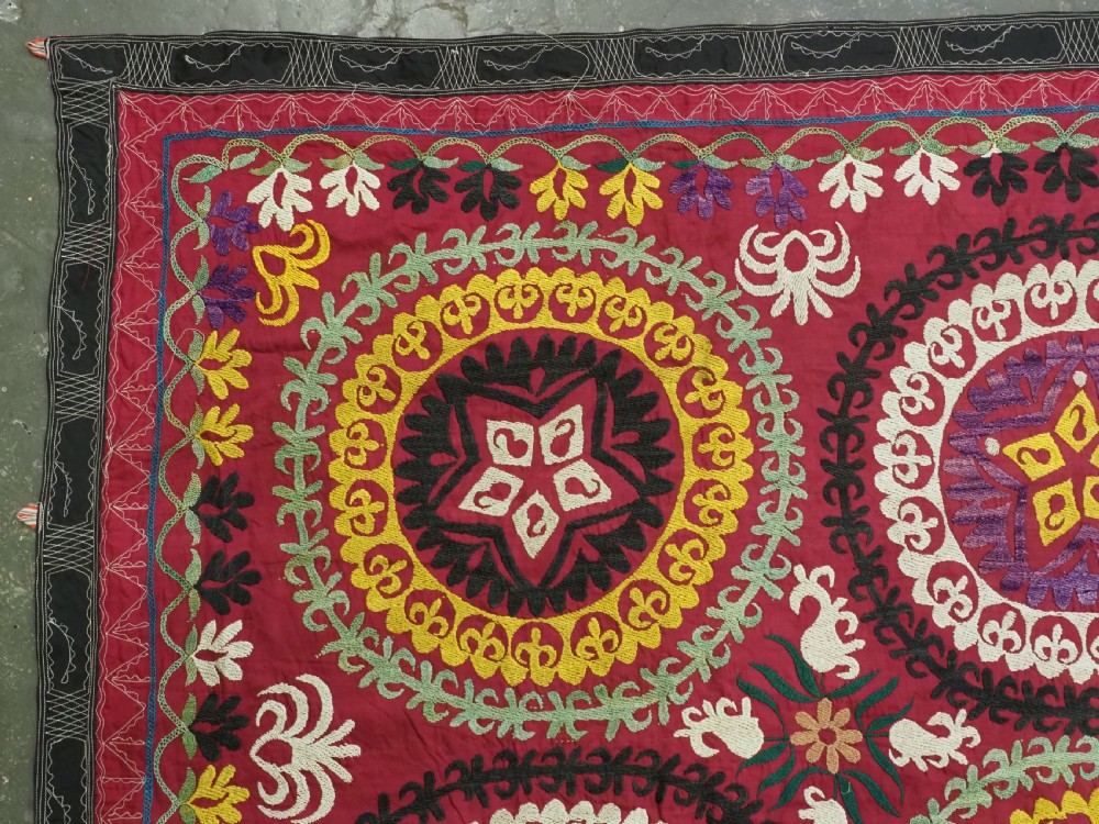 A rectangular hand-embroidered Uzbek suzani textile featuring circular solar medallions with central stars in shades of yellow, purple, white, and red. View V