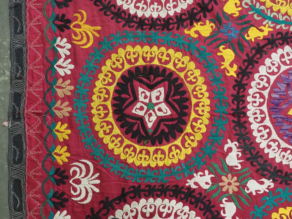A rectangular hand-embroidered Uzbek suzani textile featuring circular solar medallions with central stars in shades of yellow, purple, white, and red. View VI
