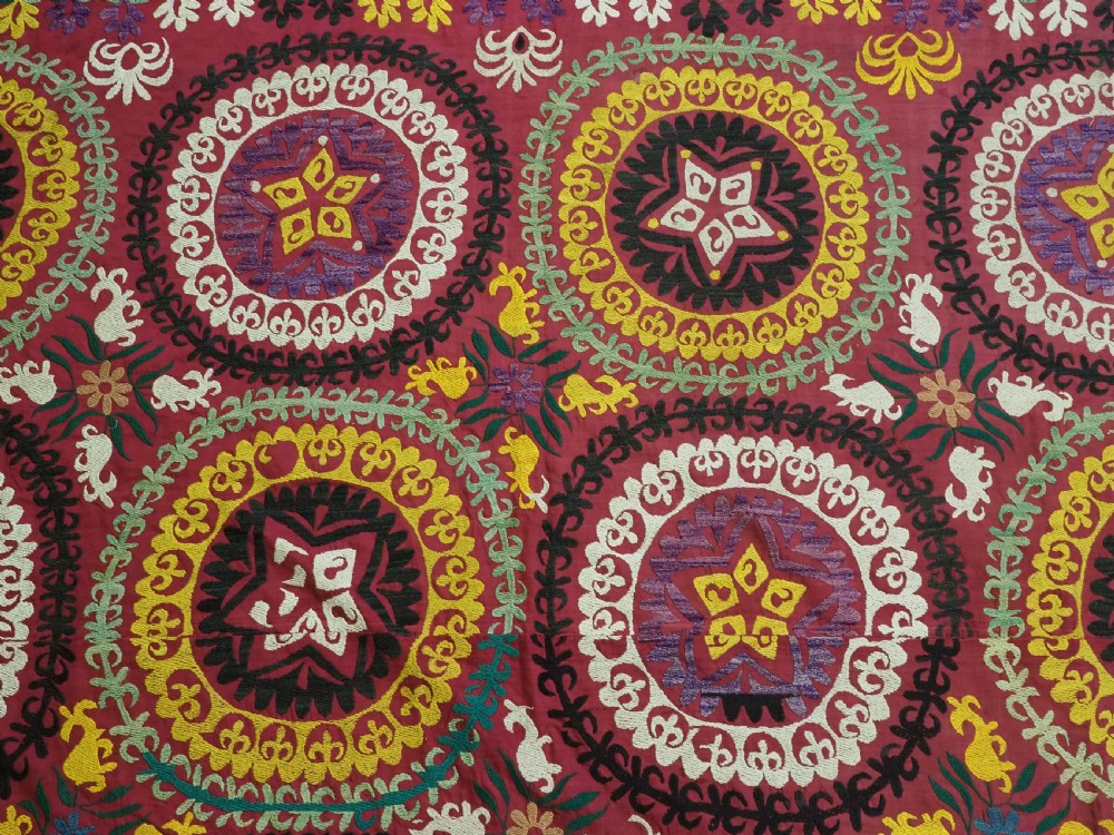 A rectangular hand-embroidered Uzbek suzani textile featuring circular solar medallions with central stars in shades of yellow, purple, white, and red. View VII