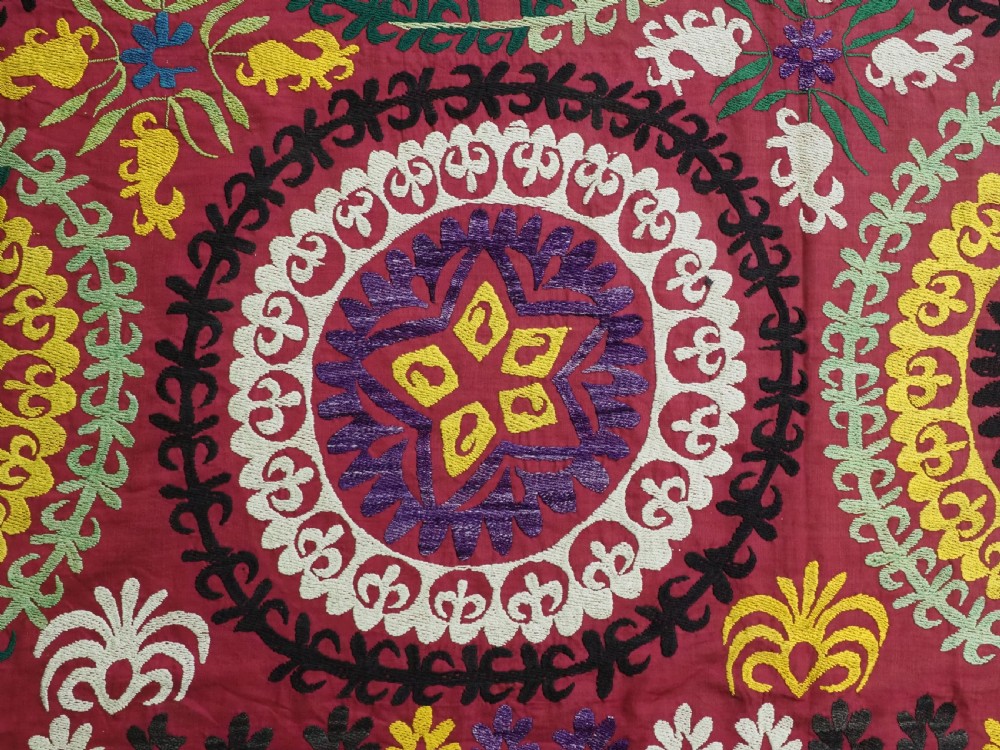 A rectangular hand-embroidered Uzbek suzani textile featuring circular solar medallions with central stars in shades of yellow, purple, white, and red. View IX