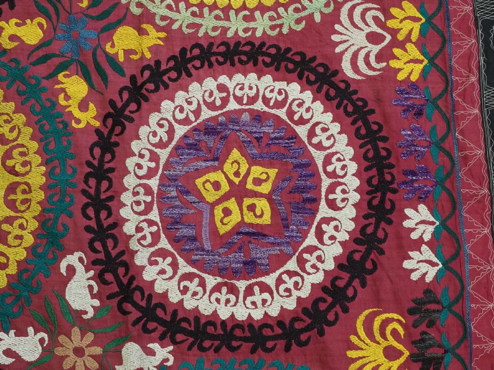 A rectangular hand-embroidered Uzbek suzani textile featuring circular solar medallions with central stars in shades of yellow, purple, white, and red. View X