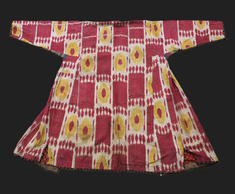 An antique T-shaped Uzbek silk ikat robe featuring geometric motifs in magenta, yellow, and off-white.