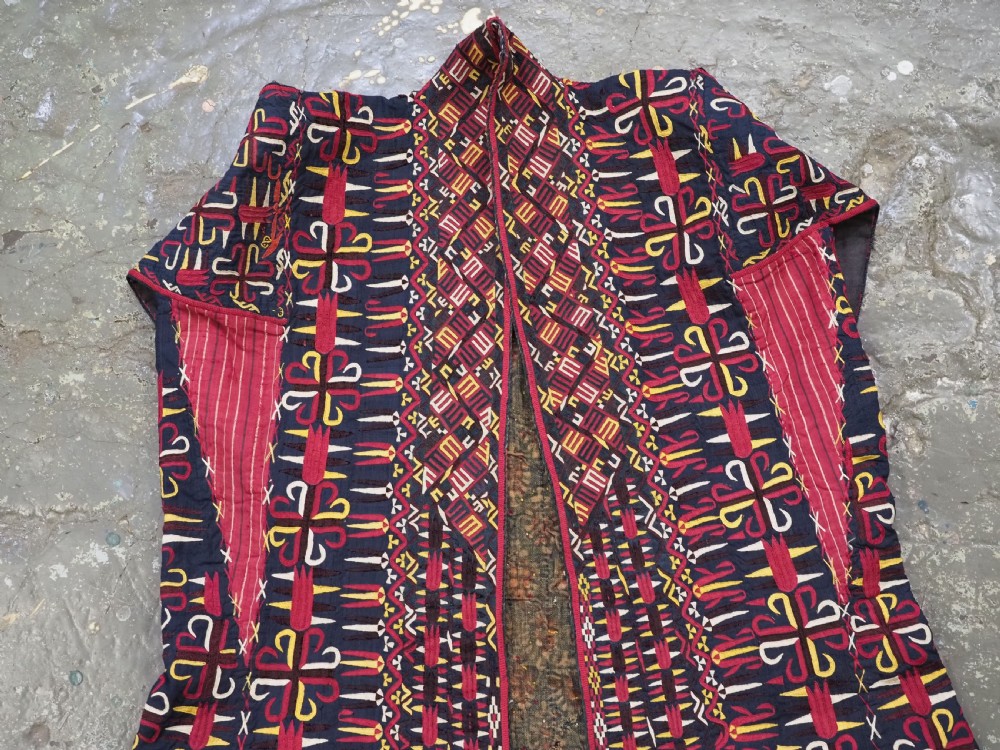 An antique 19th-century Turkmen chyrpy ceremonial coat featuring dense red, yellow, and white silk hand embroidery on a dark base with fringed borders. View X