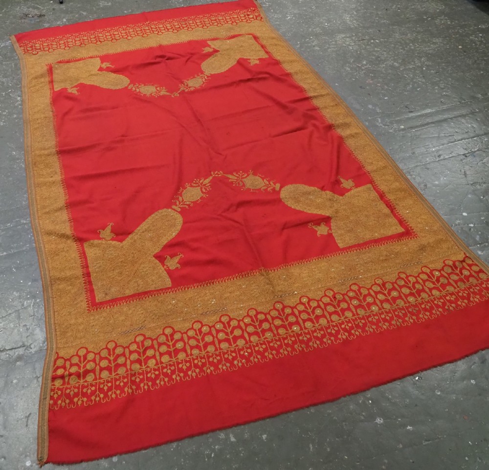 A rectangular red wool shawl with extensive gold-coloured needlework along the borders and corner motifs. View II