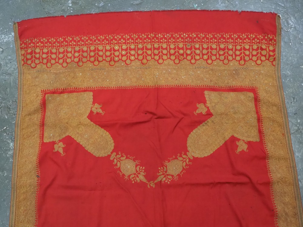 A rectangular red wool shawl with extensive gold-coloured needlework along the borders and corner motifs. View III