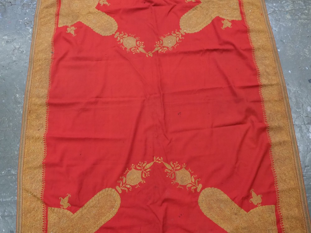 A rectangular red wool shawl with extensive gold-coloured needlework along the borders and corner motifs. View IV