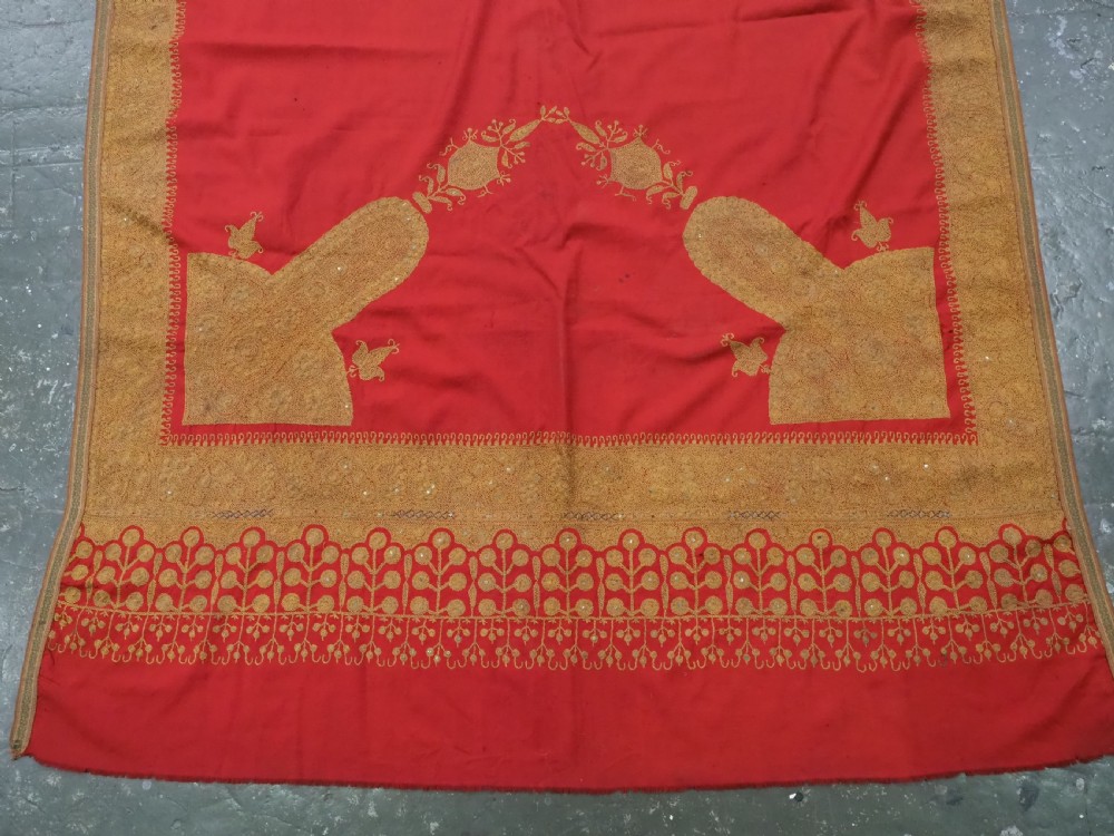 A rectangular red wool shawl with extensive gold-coloured needlework along the borders and corner motifs. View V