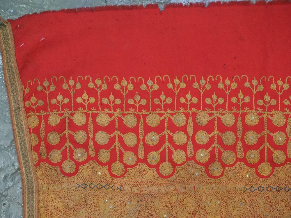 A rectangular red wool shawl with extensive gold-coloured needlework along the borders and corner motifs. View VI