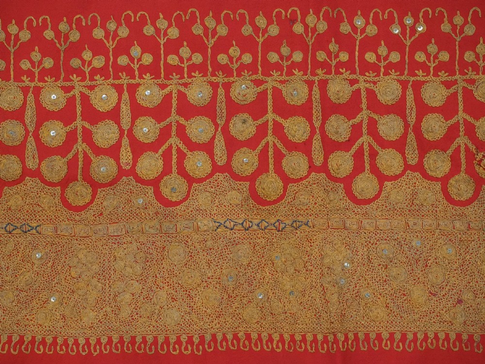 A rectangular red wool shawl with extensive gold-coloured needlework along the borders and corner motifs. View IX
