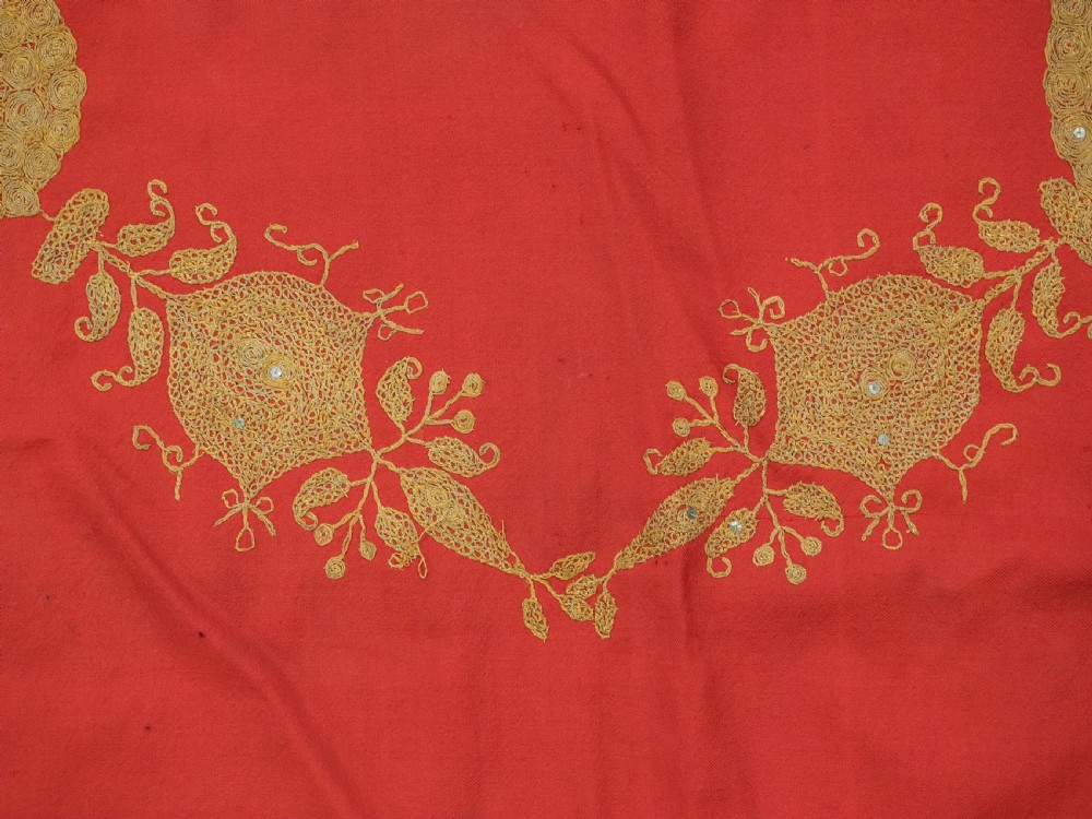 A rectangular red wool shawl with extensive gold-coloured needlework along the borders and corner motifs. View X