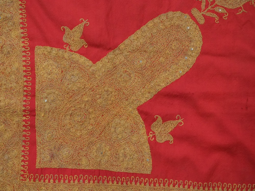 A rectangular red wool shawl with extensive gold-coloured needlework along the borders and corner motifs. View XI
