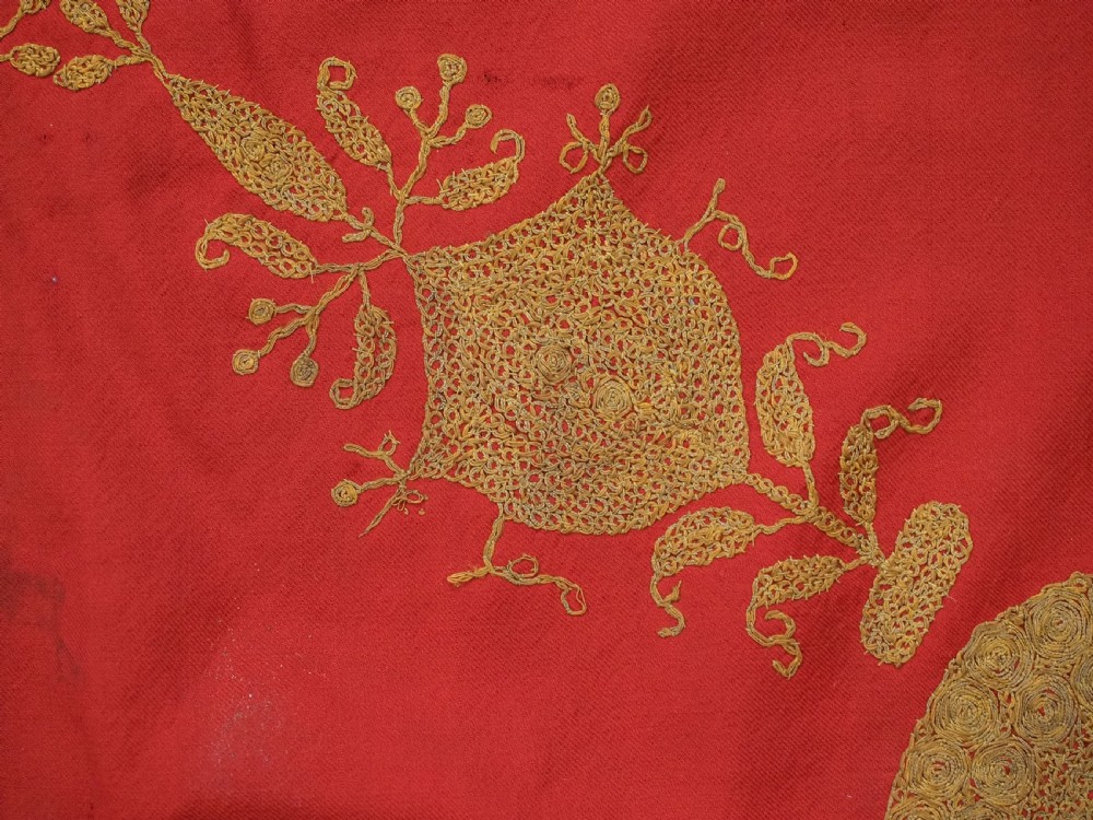 A rectangular red wool shawl with extensive gold-coloured needlework along the borders and corner motifs. View XII