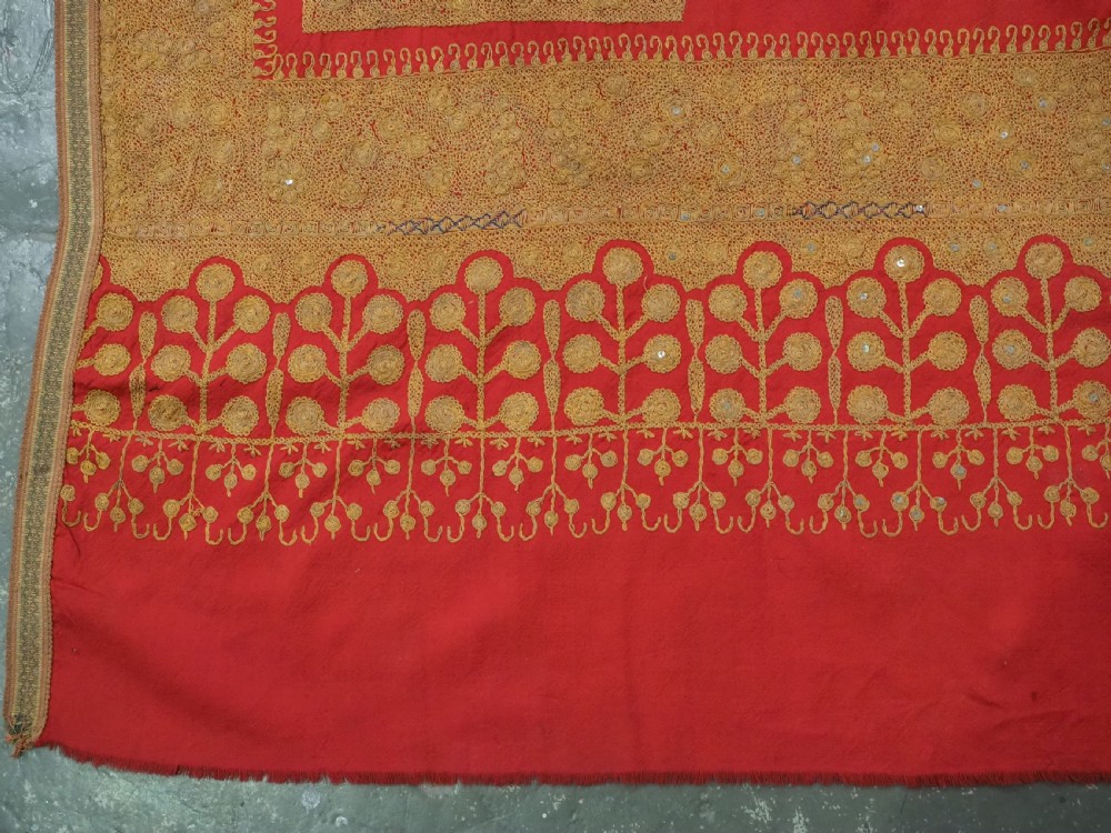 A rectangular red wool shawl with extensive gold-coloured needlework along the borders and corner motifs. View XIII
