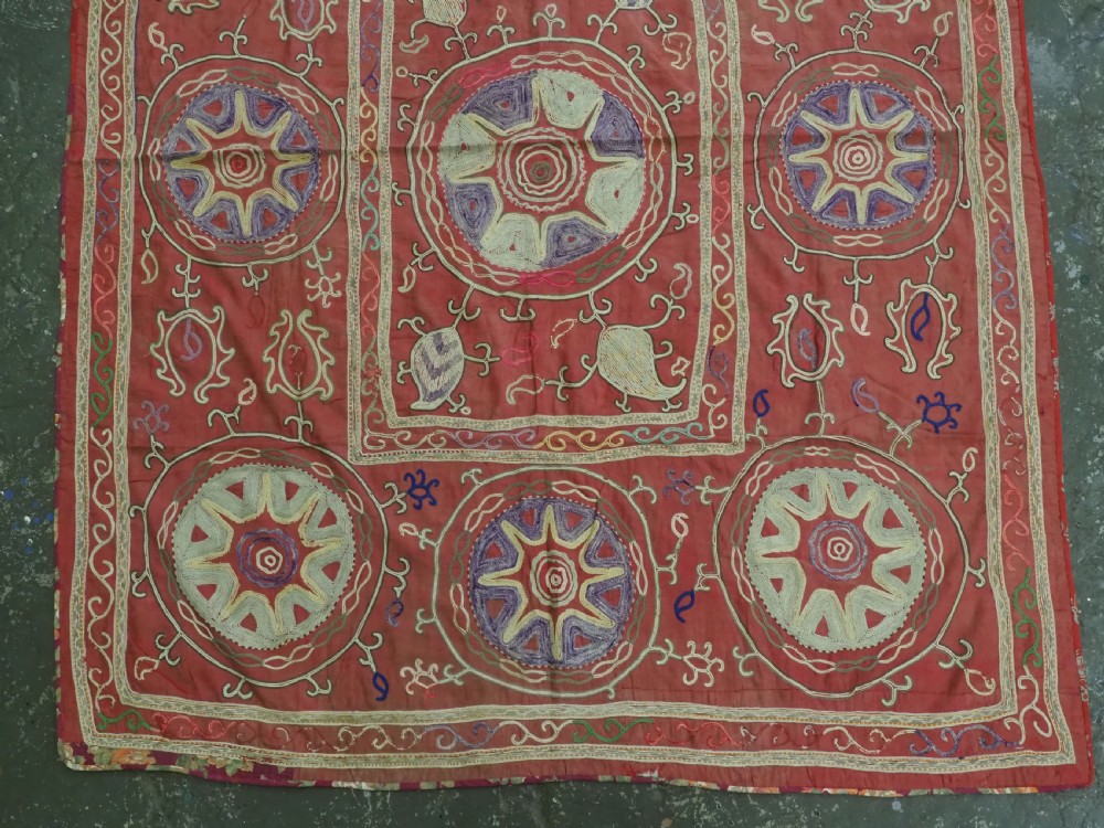 A rectangular red cotton embroidered suzani featuring geometric starburst medallions and floral scrolling borders worked in multi-coloured silk thread. View III