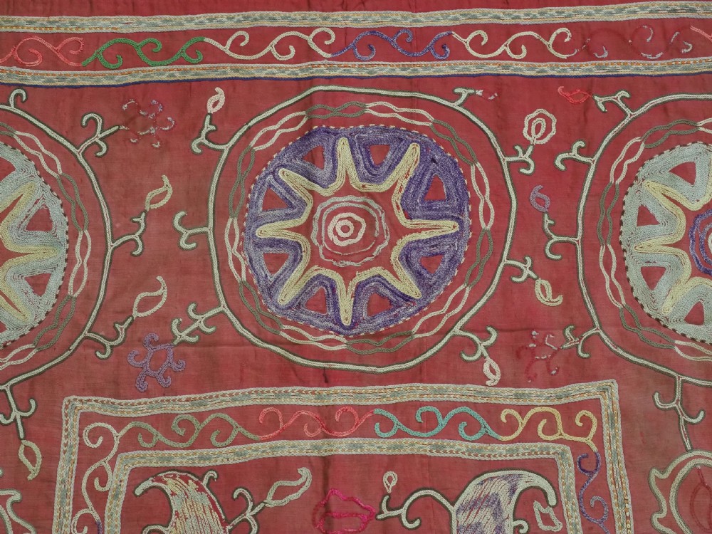 A rectangular red cotton embroidered suzani featuring geometric starburst medallions and floral scrolling borders worked in multi-coloured silk thread. View VI