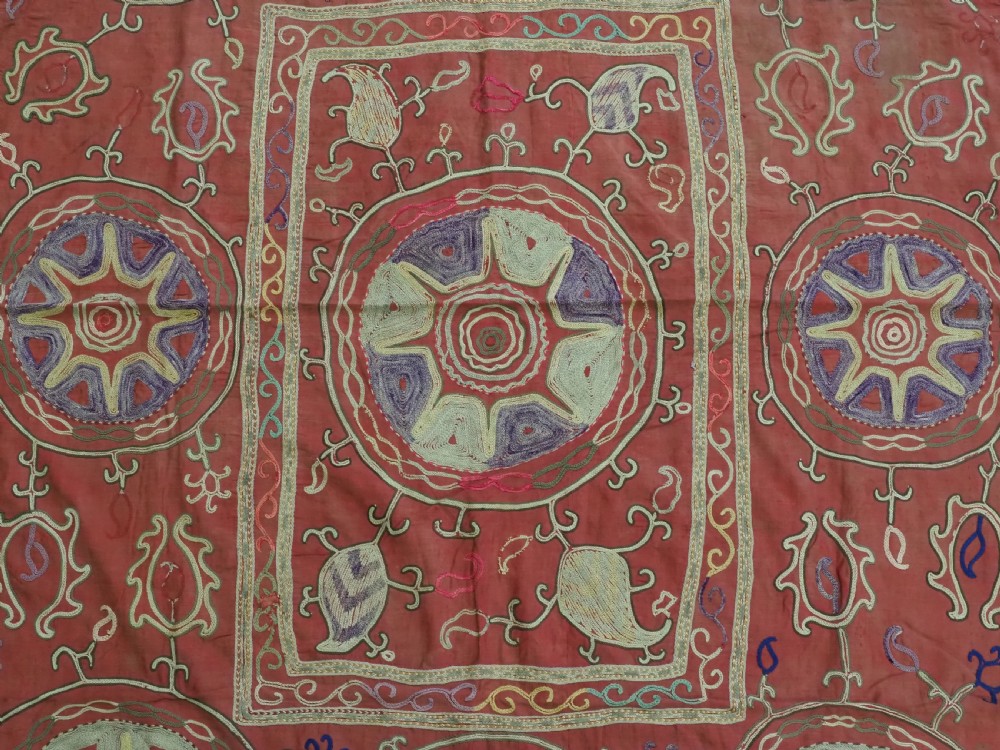 A rectangular red cotton embroidered suzani featuring geometric starburst medallions and floral scrolling borders worked in multi-coloured silk thread. View VII
