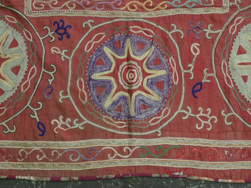 A rectangular red cotton embroidered suzani featuring geometric starburst medallions and floral scrolling borders worked in multi-coloured silk thread. View VIII