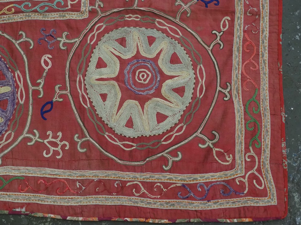 A rectangular red cotton embroidered suzani featuring geometric starburst medallions and floral scrolling borders worked in multi-coloured silk thread. View IX