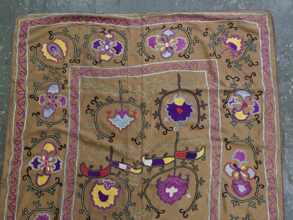 An antique Uzbek Nim Suzani textile featuring hand-embroidered floral motifs and hooked borders in purple, yellow, and blue silk threads on a tan cotton ground. View II