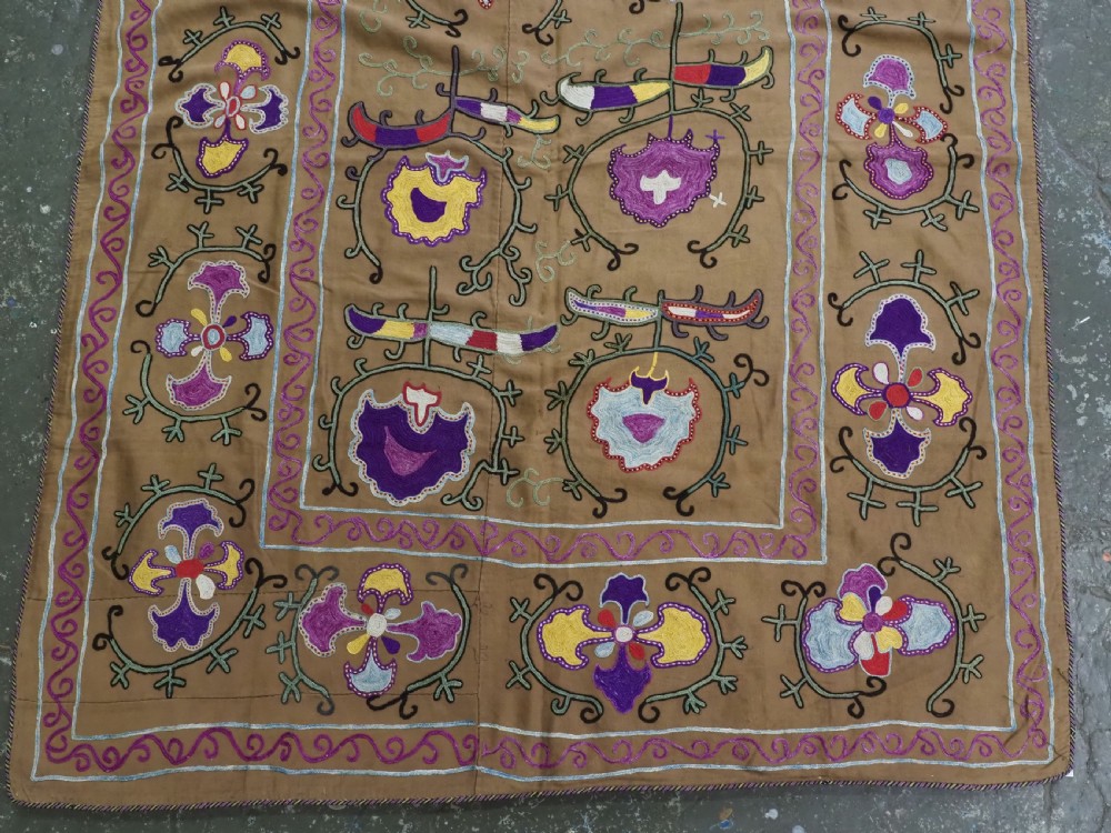 An antique Uzbek Nim Suzani textile featuring hand-embroidered floral motifs and hooked borders in purple, yellow, and blue silk threads on a tan cotton ground. View III