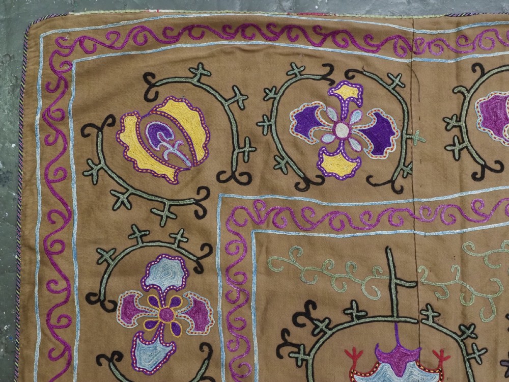 An antique Uzbek Nim Suzani textile featuring hand-embroidered floral motifs and hooked borders in purple, yellow, and blue silk threads on a tan cotton ground. View IV